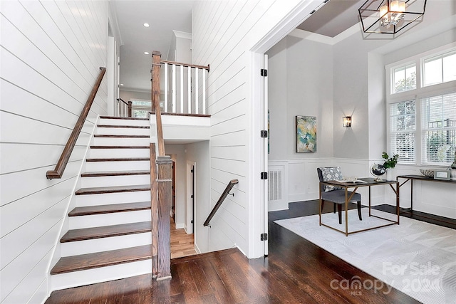 staircase with wood-type flooring, crown molding, a towering ceiling, and an inviting chandelier