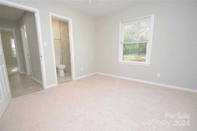 unfurnished bedroom featuring light colored carpet and connected bathroom