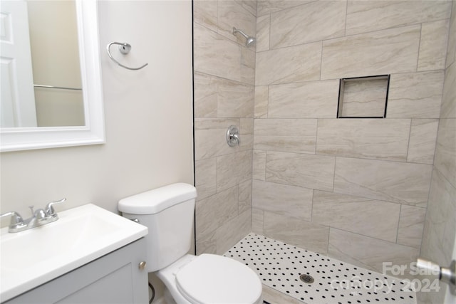 bathroom with a tile shower, vanity, and toilet