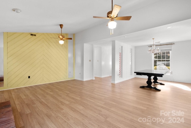 unfurnished living room featuring ceiling fan with notable chandelier, light wood-type flooring, and wood walls