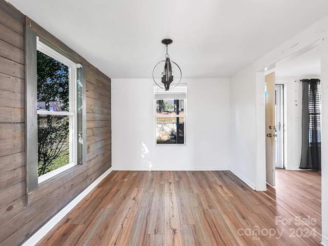 unfurnished dining area featuring a chandelier, hardwood / wood-style floors, and wood walls