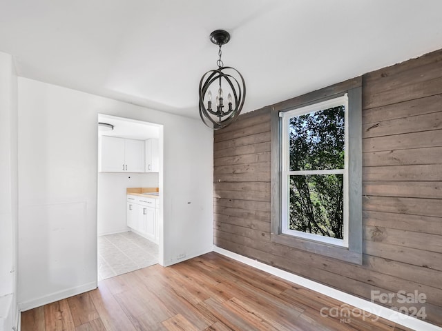 unfurnished dining area with light wood-type flooring, an inviting chandelier, and wood walls