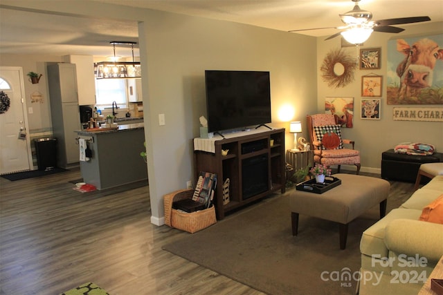 living room with ceiling fan with notable chandelier, dark wood-type flooring, and sink