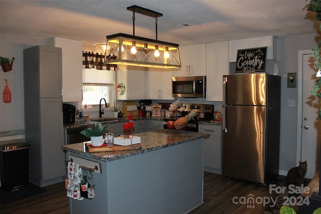 kitchen featuring pendant lighting, sink, appliances with stainless steel finishes, dark hardwood / wood-style flooring, and white cabinetry