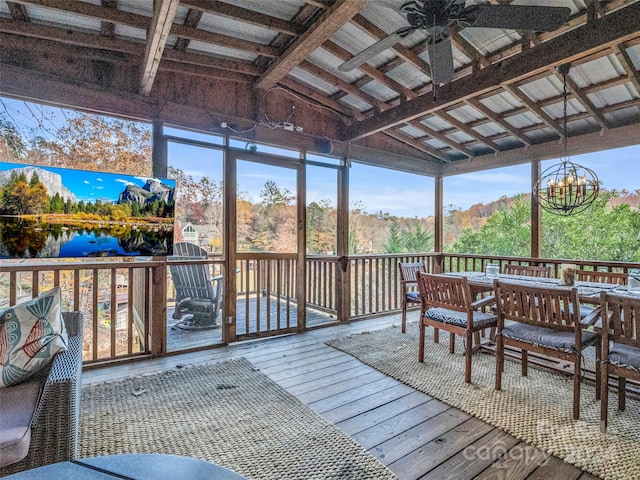 sunroom / solarium with ceiling fan with notable chandelier, vaulted ceiling with beams, and a water view