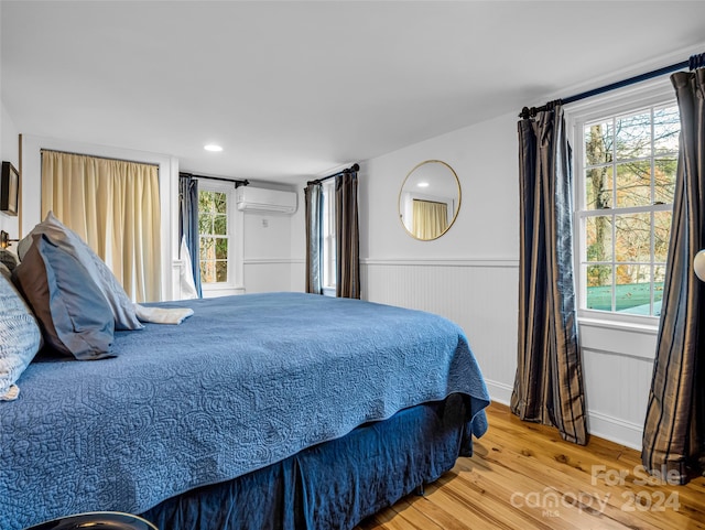 bedroom with multiple windows, wood-type flooring, and a wall mounted AC