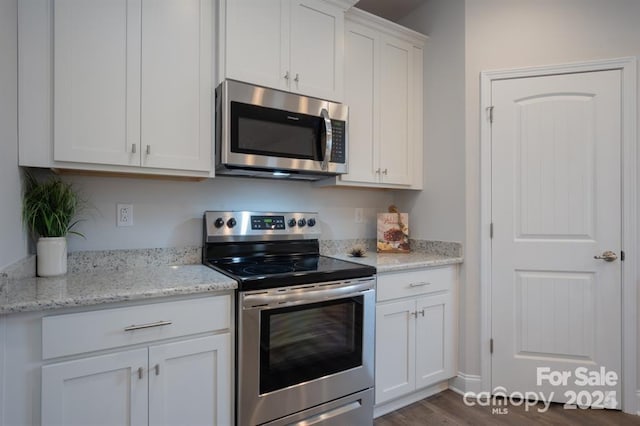 kitchen with dark wood-type flooring, appliances with stainless steel finishes, white cabinetry, and light stone counters