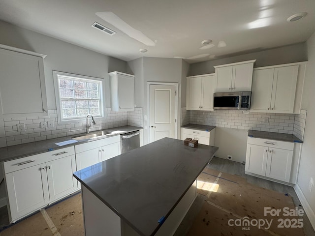 kitchen with stainless steel appliances, dark countertops, a sink, and visible vents