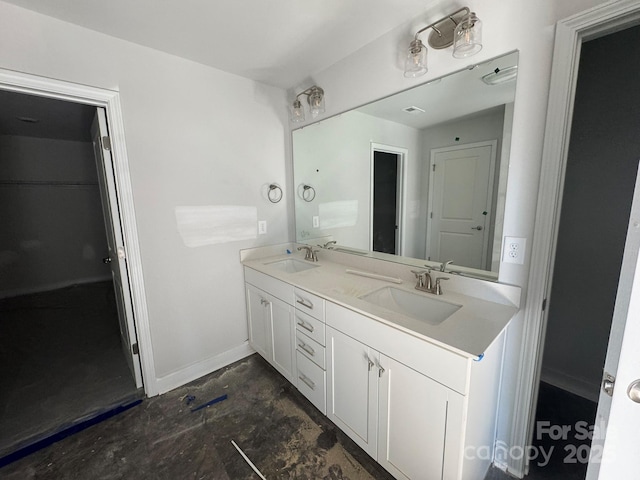 bathroom with double vanity, baseboards, a walk in closet, and a sink