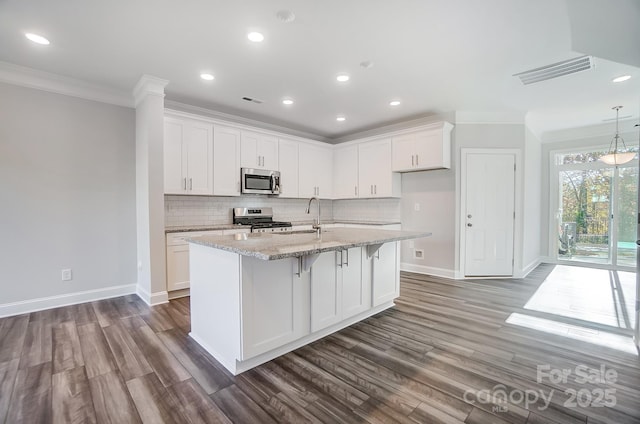 kitchen with white cabinets, light stone counters, stainless steel appliances, and an island with sink