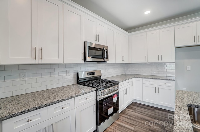 kitchen with decorative backsplash, dark wood finished floors, white cabinets, appliances with stainless steel finishes, and light stone counters