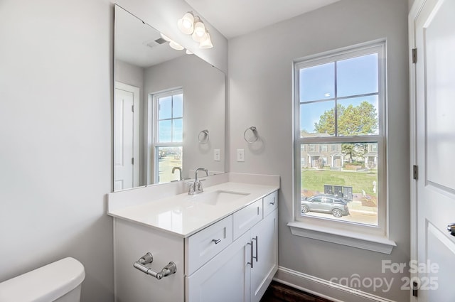 half bath featuring toilet, baseboards, visible vents, and vanity