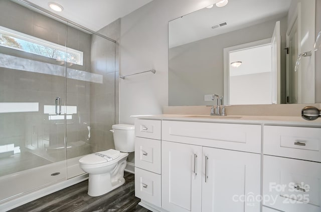 bathroom with toilet, wood finished floors, visible vents, vanity, and a stall shower