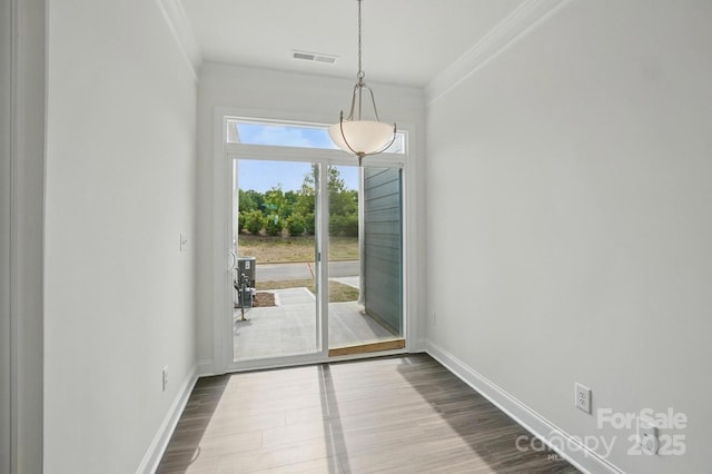 unfurnished dining area featuring baseboards, ornamental molding, dark wood-style flooring, and visible vents
