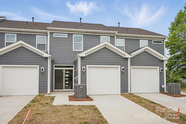 multi unit property featuring a garage, a shingled roof, driveway, and central AC unit