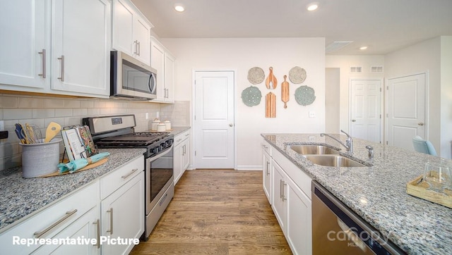 kitchen with light stone counters, stainless steel appliances, sink, light hardwood / wood-style floors, and white cabinetry