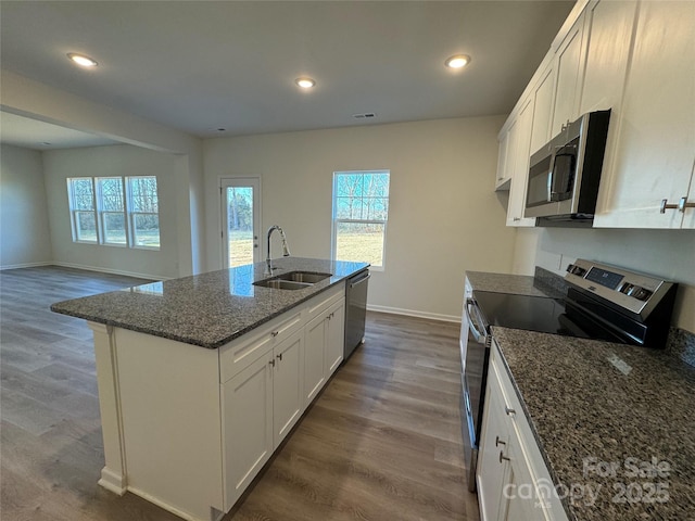 kitchen with white cabinetry, sink, stainless steel appliances, an island with sink, and dark stone counters