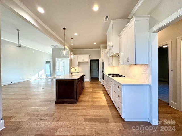 kitchen featuring a center island with sink, white cabinets, ornamental molding, decorative light fixtures, and light hardwood / wood-style floors