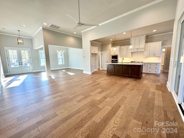 kitchen with white cabinetry, sink, french doors, light hardwood / wood-style floors, and a kitchen island with sink