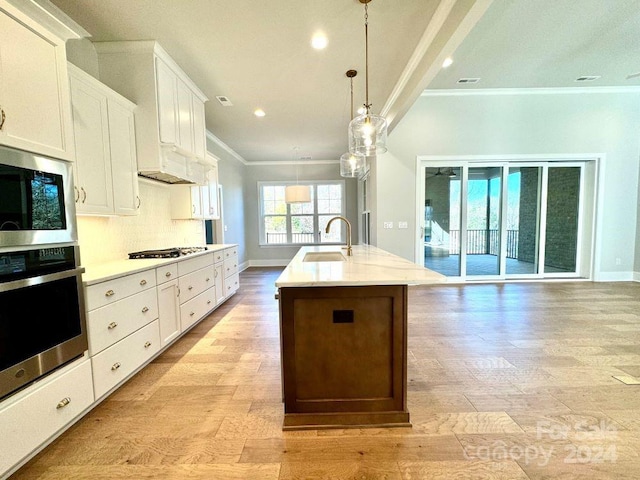 kitchen with white cabinetry, sink, stainless steel appliances, pendant lighting, and a center island with sink