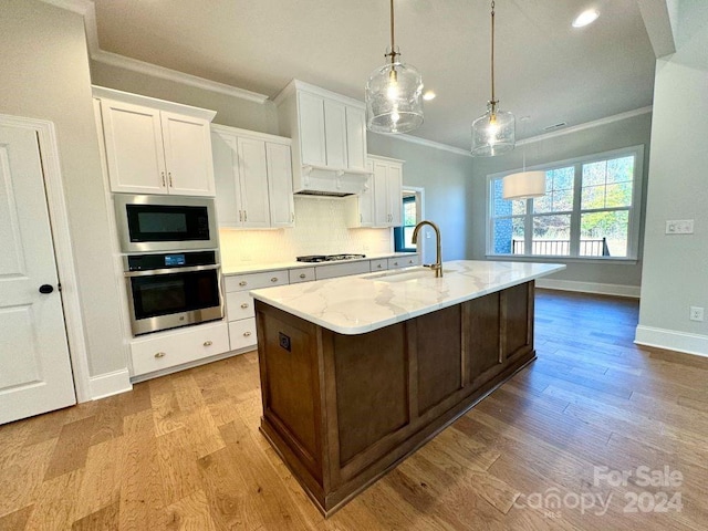 kitchen with decorative light fixtures, white cabinetry, stainless steel appliances, and an island with sink