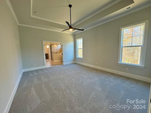 unfurnished bedroom featuring carpet, ensuite bath, ornamental molding, a raised ceiling, and ceiling fan