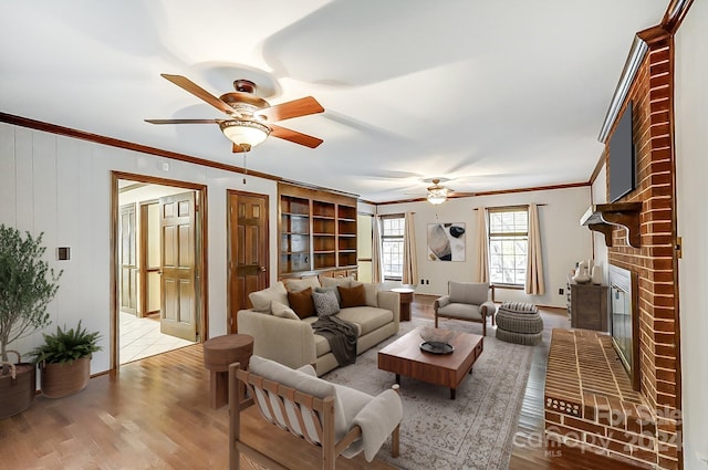 living room with a fireplace, ceiling fan, crown molding, and light hardwood / wood-style flooring