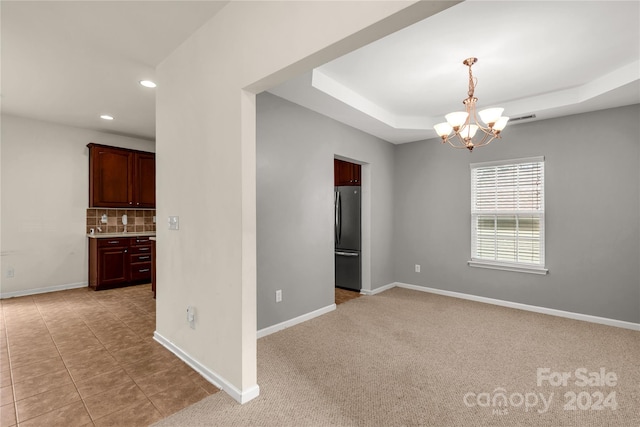 carpeted empty room featuring a raised ceiling and an inviting chandelier