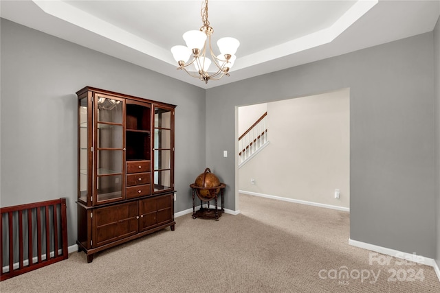 carpeted empty room featuring a raised ceiling and a chandelier