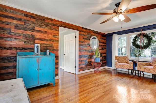 sitting room with wood walls, hardwood / wood-style floors, ceiling fan, and crown molding