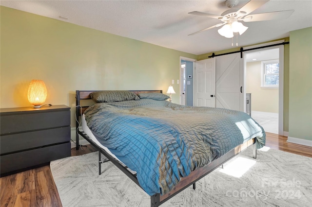 bedroom featuring a barn door, ceiling fan, hardwood / wood-style floors, and a textured ceiling