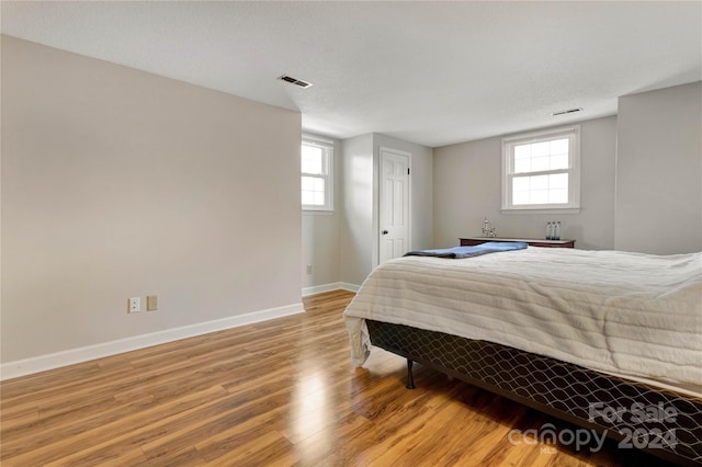 bedroom with wood-type flooring, a textured ceiling, and multiple windows