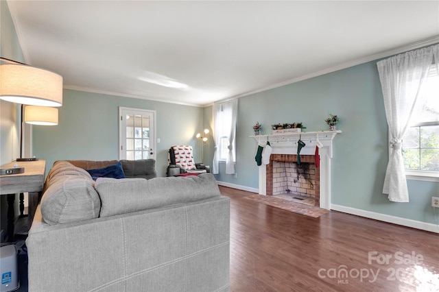 living room with a healthy amount of sunlight, ornamental molding, dark wood-type flooring, and a brick fireplace