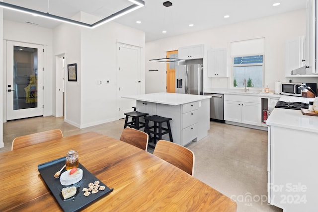 kitchen with a kitchen breakfast bar, stainless steel appliances, sink, white cabinets, and a center island