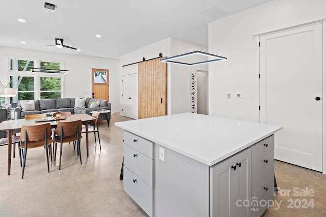 kitchen featuring gray cabinetry, ceiling fan, a barn door, a center island, and hanging light fixtures