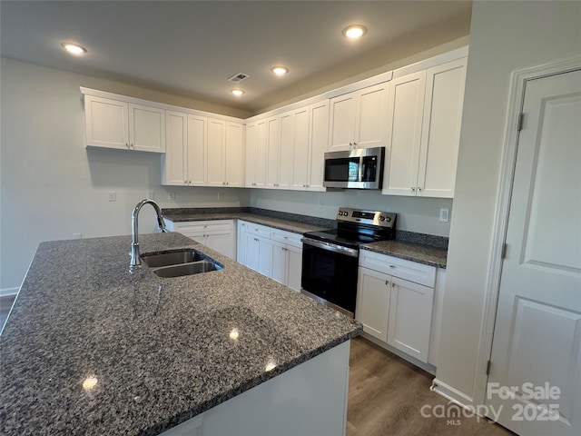 kitchen with stainless steel appliances, white cabinetry, dark stone counters, and sink