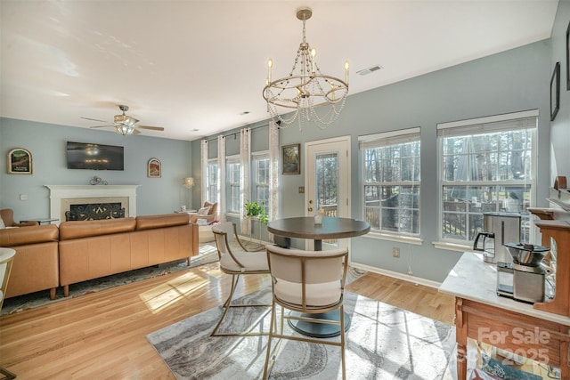 dining space with ceiling fan with notable chandelier, light hardwood / wood-style flooring, and a wealth of natural light