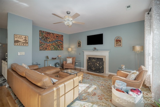 living room featuring a premium fireplace, ceiling fan, and light wood-type flooring