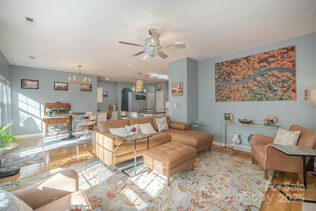 living room with ceiling fan with notable chandelier and light hardwood / wood-style flooring