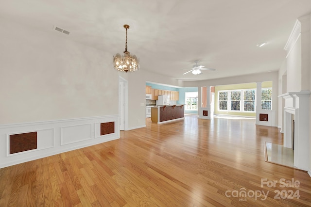 unfurnished living room featuring ceiling fan with notable chandelier and light wood-type flooring