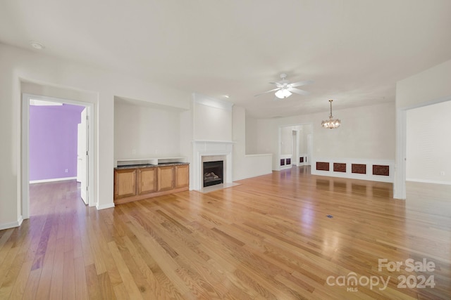 unfurnished living room with a fireplace, light hardwood / wood-style flooring, and ceiling fan with notable chandelier