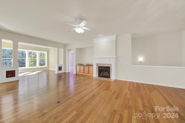 unfurnished living room with ceiling fan, a large fireplace, and light hardwood / wood-style floors