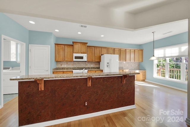 kitchen with light wood-type flooring, white appliances, decorative light fixtures, and washing machine and dryer