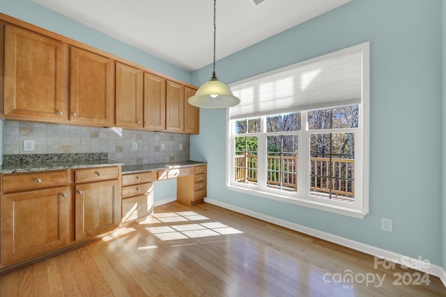 kitchen with light stone countertops, light hardwood / wood-style flooring, backsplash, decorative light fixtures, and built in desk