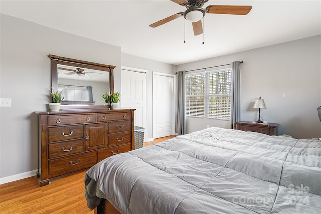 bedroom featuring light hardwood / wood-style flooring, ceiling fan, and multiple closets