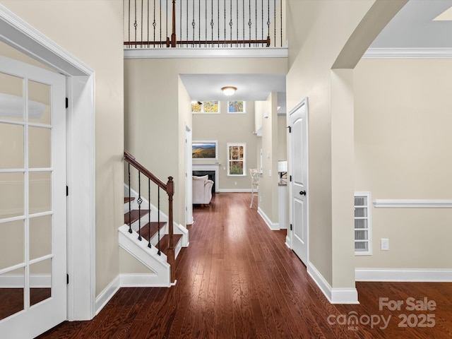 foyer entrance with a high ceiling, dark wood-type flooring, and crown molding