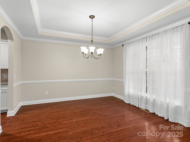 unfurnished room with ornamental molding, dark wood-type flooring, a raised ceiling, and a chandelier