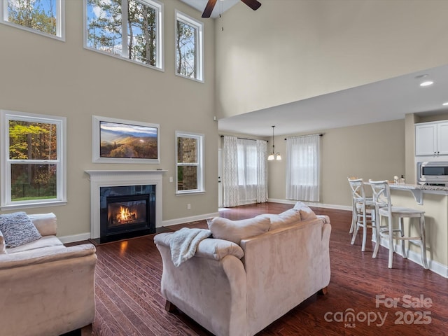 living room featuring a high ceiling, ceiling fan with notable chandelier, plenty of natural light, and dark wood-type flooring