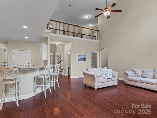 living room with ceiling fan, dark wood-type flooring, and a towering ceiling