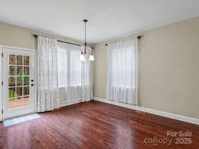 unfurnished dining area featuring a notable chandelier and dark hardwood / wood-style flooring